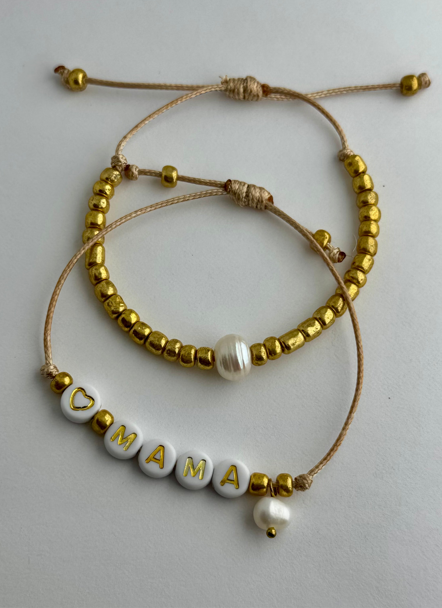 MAMA - Dúo de pulseras en hilo hecha a mano color dorado con la palabra MAMÁ, perlas de agua dulce y mostacillas.