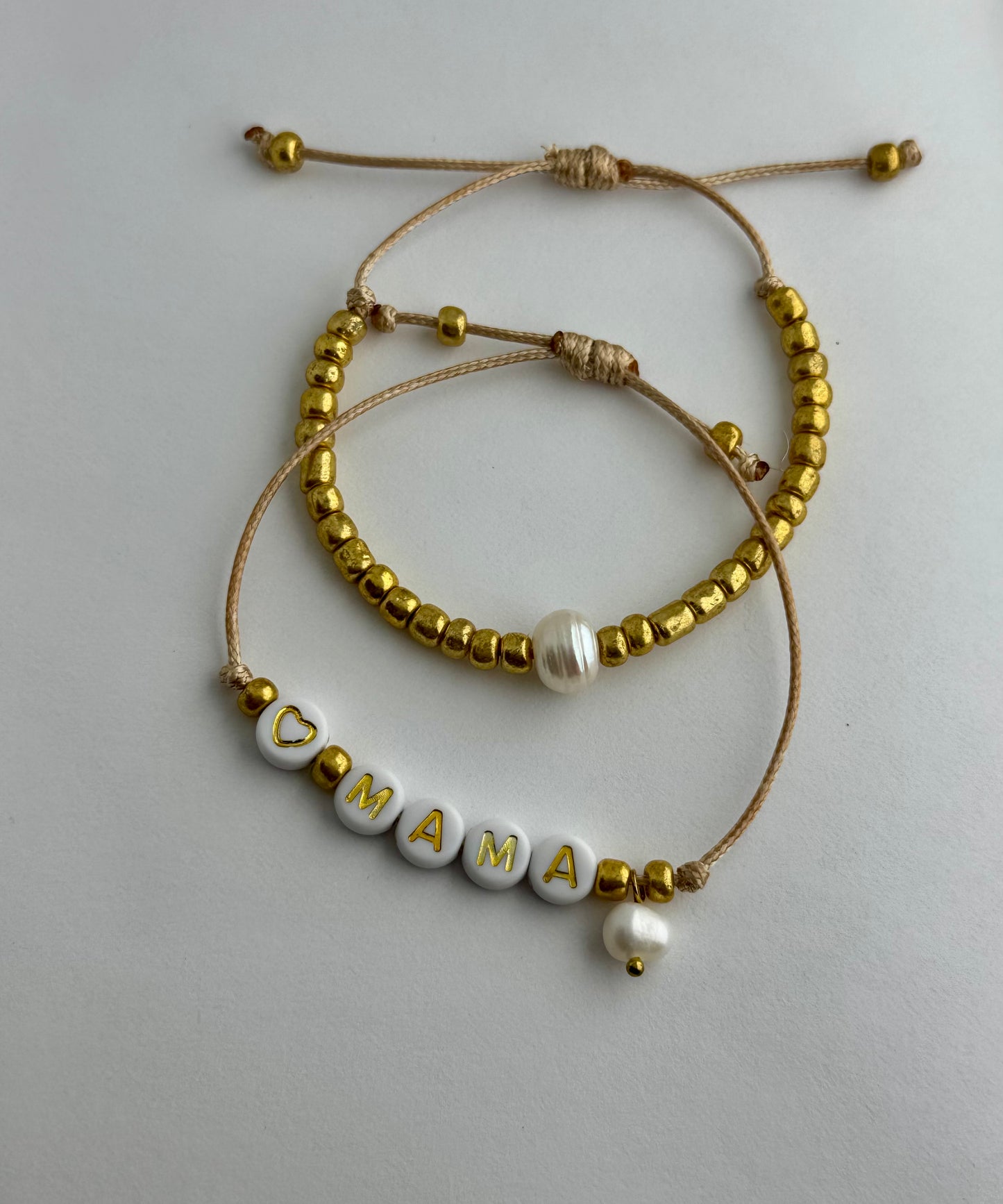 MAMA - Dúo de pulseras en hilo hecha a mano color dorado con la palabra MAMÁ, perlas de agua dulce y mostacillas.
