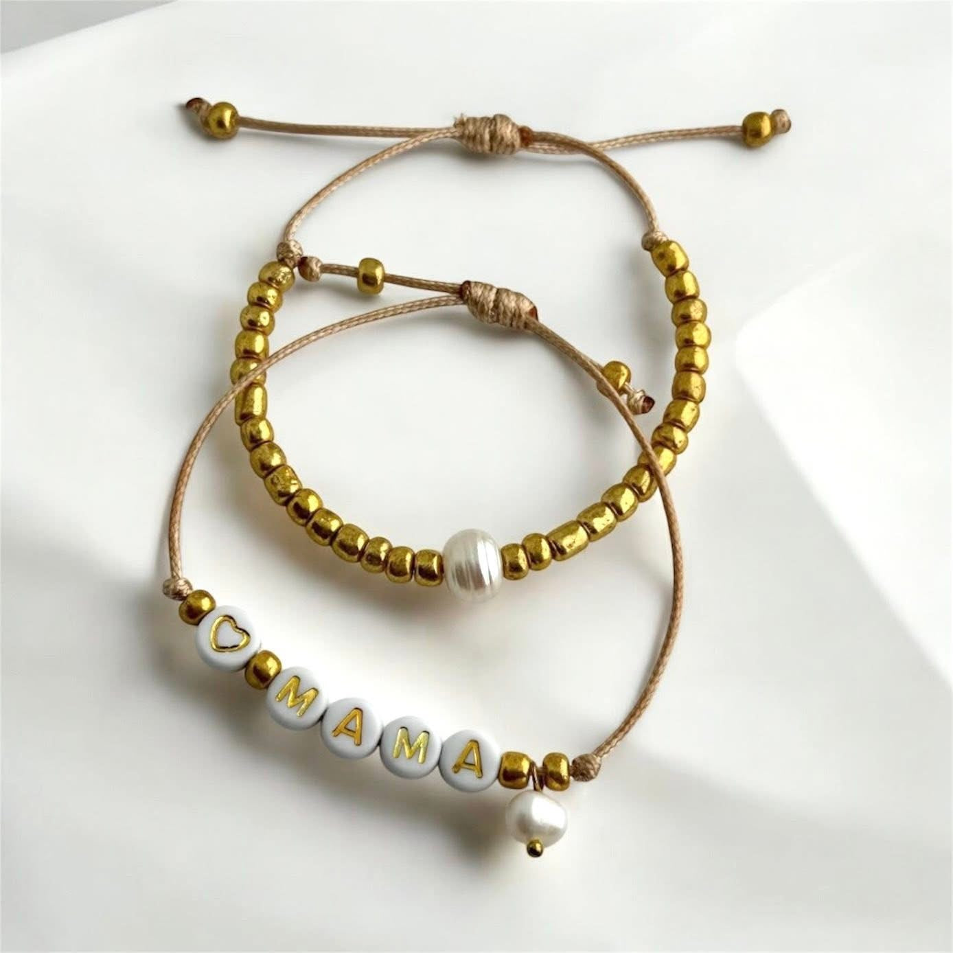MAMA - Dúo de pulseras en hilo hecha a mano color dorado con la palabra MAMÁ, perlas de agua dulce y mostacillas.